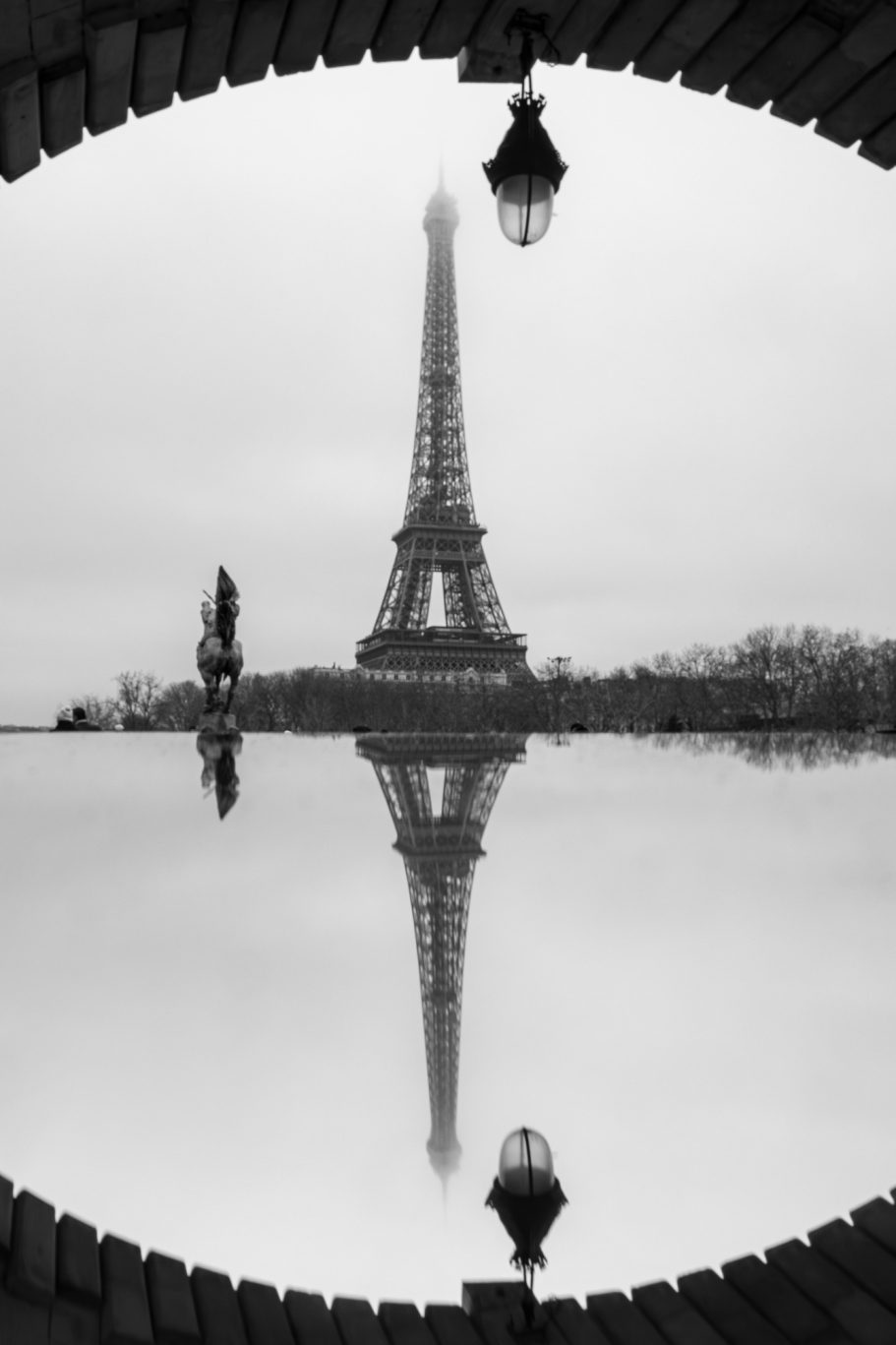 Eiffel Tower in Paris, reflected in the water under an arch.