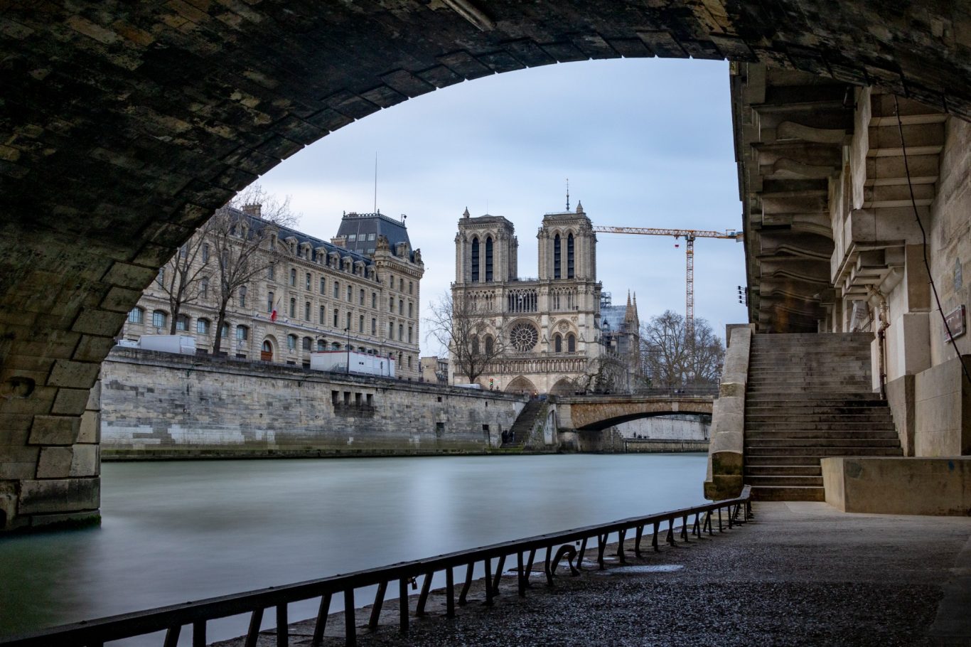 View of Notre-Dame from under a bridge on the banks of the Seine, with running water.