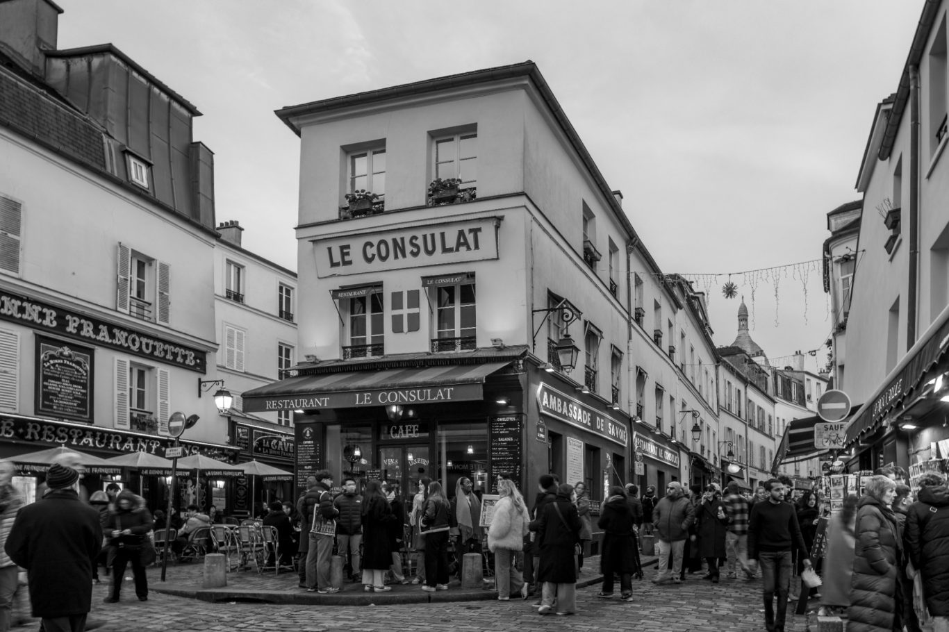 Street with people and the restaurant "Le Consulat" in a historic setting.