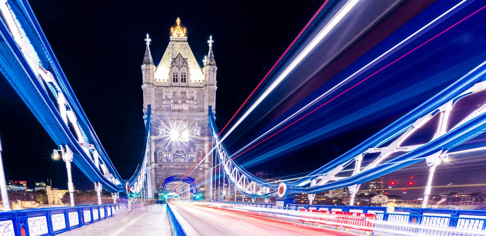 Lights Over the Thames Illuminated Tower Bridge at night with blurred lights in the foreground.