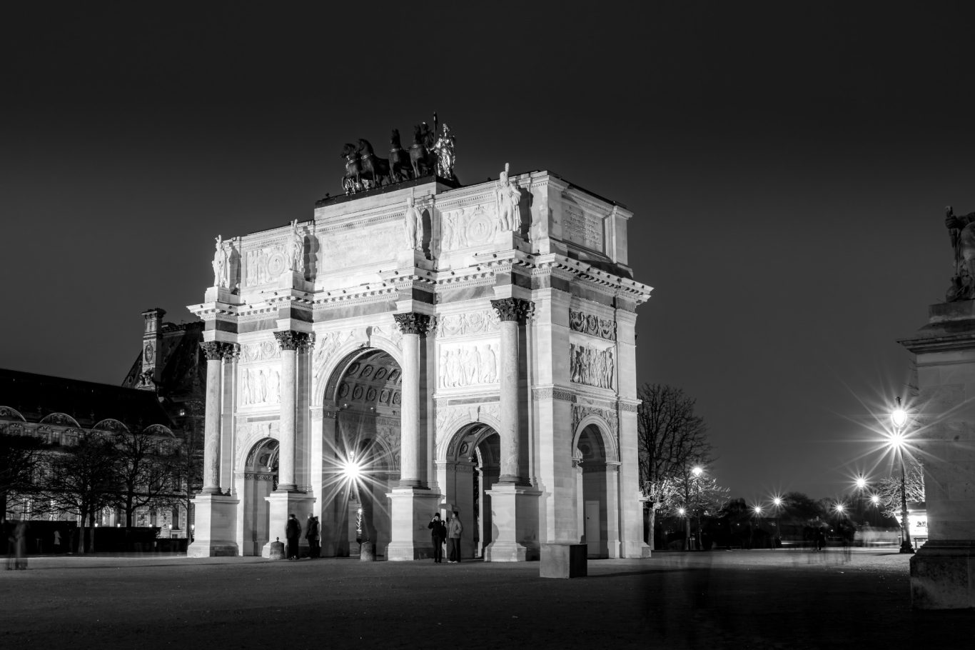 Black and white photo of a monumental arch at night in Paris.