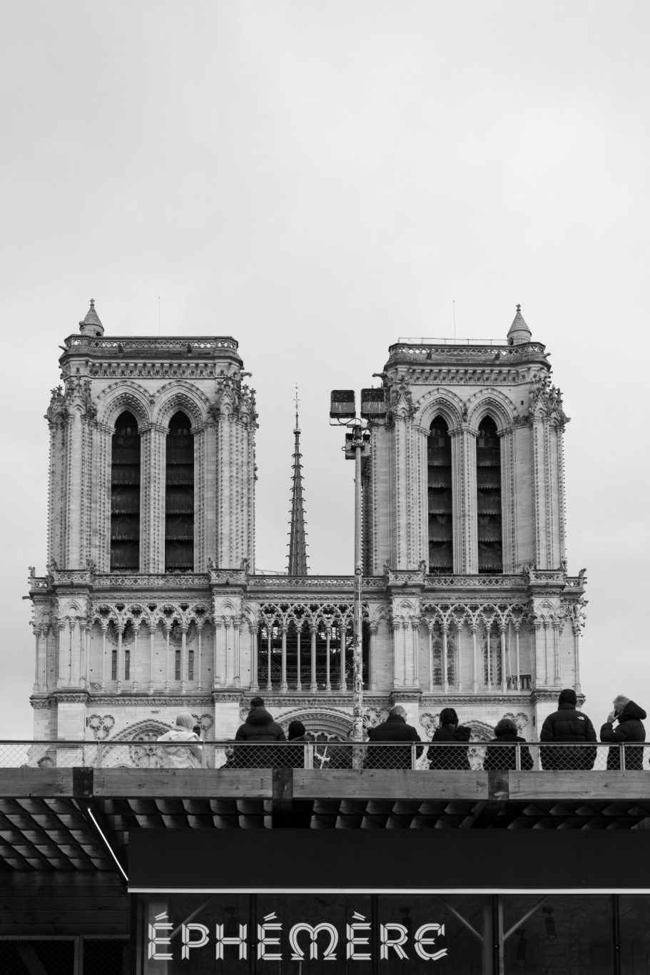 The towers of Notre-Dame Cathedral above the edge of a sign, photographed in black and white.