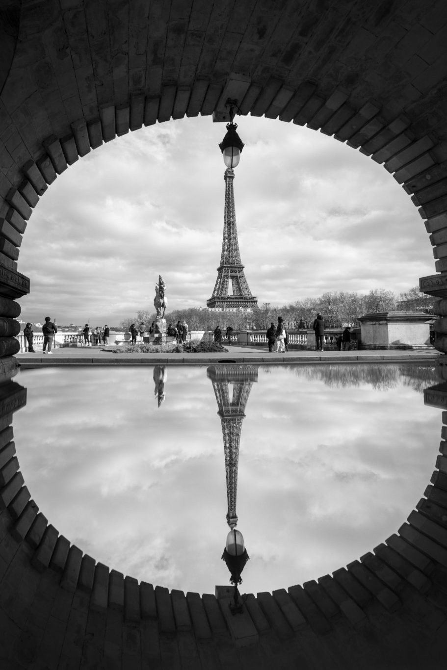 Eiffel Tower in black and white, reflected in the water under an arch.