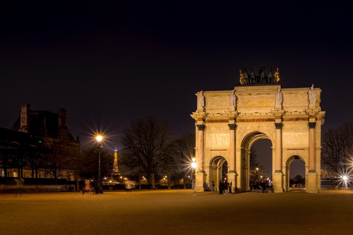 Arch with illuminated columns, surrounded by night-time scenery and trees.