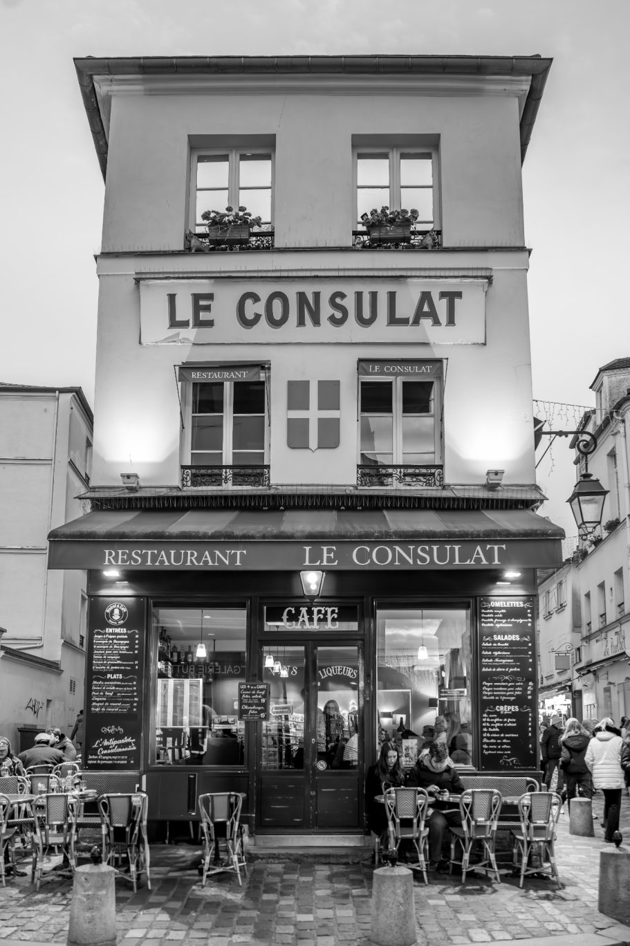 Black and white photo of a café called "Le Consulat" in a city street.