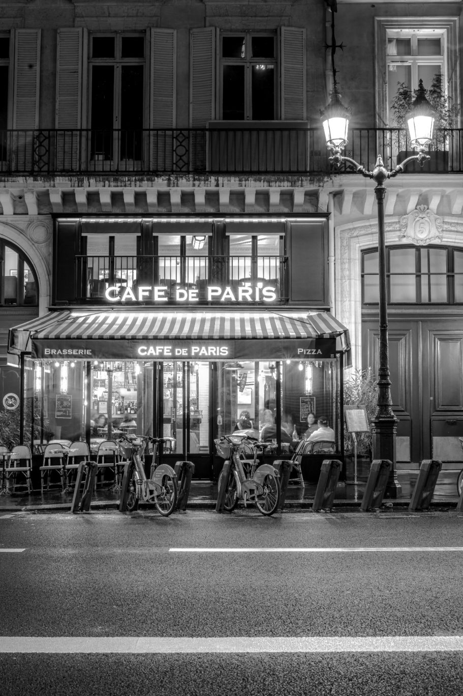 Black and white shot of a café with tables outside in a city street.