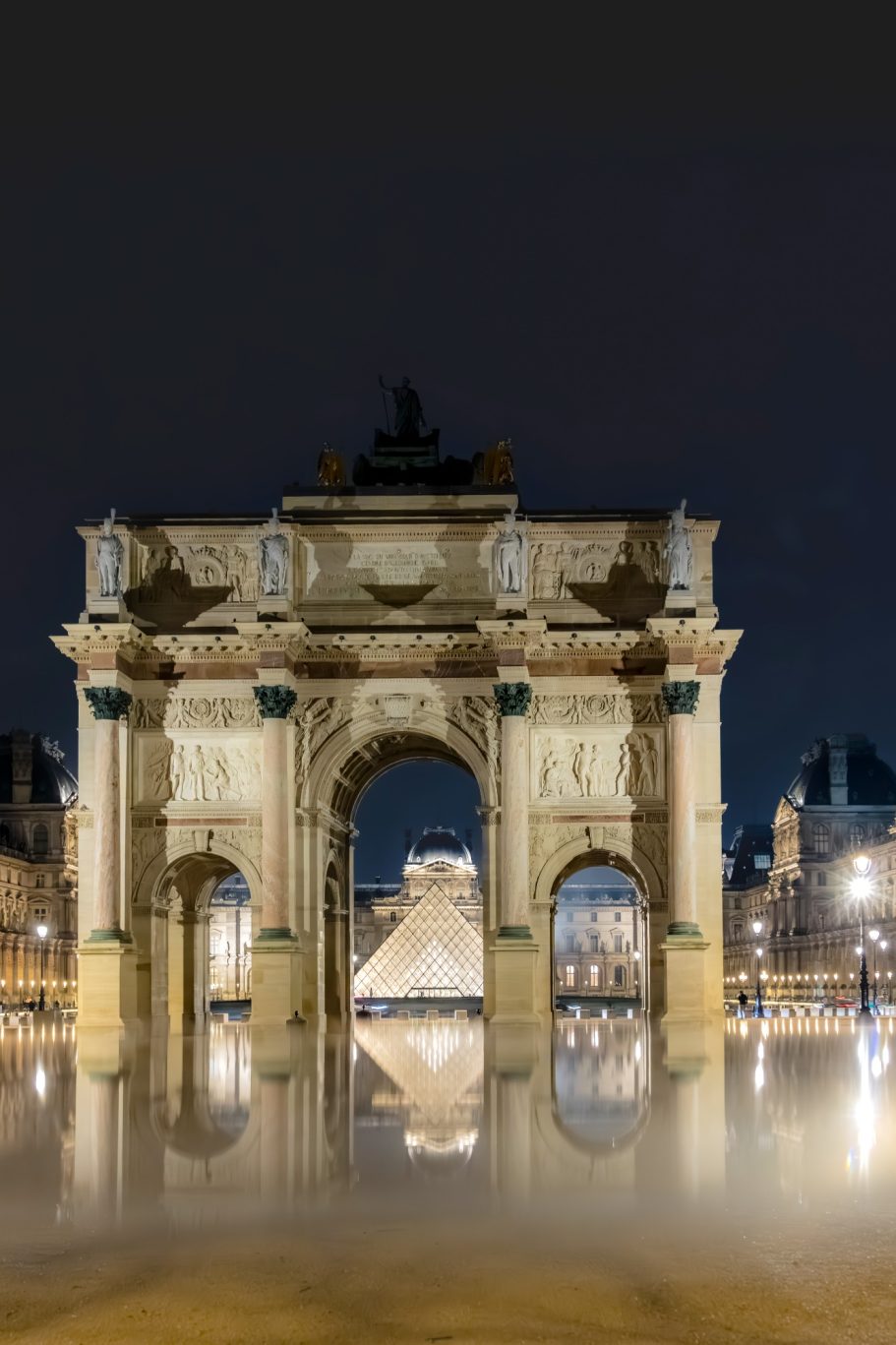 Arch with historical details and reflection in the water at night.